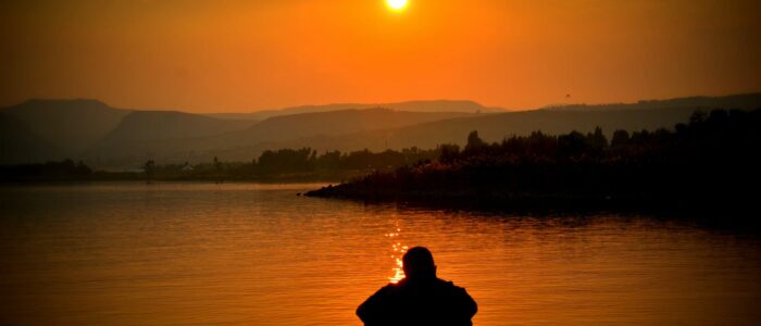 silhouette of person sitting beside body of water